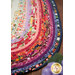 A stylized close up on the Jelly Roll Rug demonstrating print and color details on the fabrics; coordinating flowers peek into frame from the lower right corner.