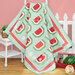 The completed Watermelon Patchwork quilt in colorful aqua, pink, red, and green fabrics featuring watermelon slices, artfully draped over a white ladder in front of a pink wall, staged with coordinating decor and watermelon slices.