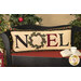 The completed pillow colored in festive A Vintage Christmas fabrics, staged on a black and red bench with a cup of tea and a book, in front of a Christmas tree set.