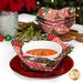 The completed bowl cozy colored in red and green fabrics from the Berry & Pine collection by Moda Fabrics, staged on a red plate and holding a white bowl with a warm pie inside. The other bowl cozies and coordinating decor can be seen in the background.