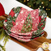 Three nested bowl cozies in red and green fabrics, staged on a wooden cutting board on a white table.