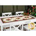 A shot of the table runner staged on a white table with a stack of coordinating gold-rimmed plates topped with cloth napkins, and a decorated Christmas tree in the background.