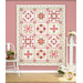 A quilt featuring a floral and geometric pattern in red, pink, and green against a pink wall.