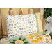 A full shot of the Magic Pillowcase in white, yellow, and green, staged on a bed with a matching patchwork quilt and elephant plushie in a cabin setting.