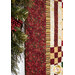 A super close up on the border and inner borders of the quilt, showing details on the rich red holly themed fabric as a sparkling garland peeks into frame from the left side.