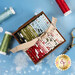 A wooden box filled with colorful fabric strips tied with a ribbon, surrounded by spools of thread on a blue snowy background.