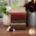 A stack of the fabrics included in the Hearth & Home collection with vases and flowers and a window and thread.