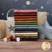 A stack of the fabrics included in the Seeing Stars collection, with a star and candles and a lantern and thread.