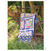 A vintage bicycle decorated with a patchwork quilt, leaning against a tree in a grassy area.