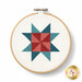 The completed pinwheel star cross stitch project made with the thread set, in a wooden hoop and isolated on a white background.