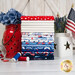 A stack of the fabrics included in the Celebrate the USA collection, with a jar and flowers and a flag and buttons and thread.