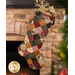 The completed Fast Fusible Patchwork Stocking colored in the A Vintage Christmas collection, hung on a stone fireplace with Christmas decor and gifts peeking out of the top of the stocking.