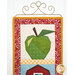 A close up on the top green apple block of the project, hung on a golden craft hanger. The top of the barn block peeks into frame from the bottom.