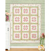 A shot of the completed quilt colored in pink, green, and white floral fabrics from the Shades of Romance collection, hung on a green-paneled wall and bordered by coordinating florals and décor.