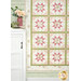 A shot of the lower left corner of the quilt staged next to a white cabinet with a vase of flowers and small sewing machine on top.