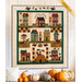The completed Autumn House BOM Quilt, featuring whimsical houses and pumpkins in saturated earth tones, displayed on a wooden wall with autumn decor.
