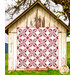 The completed Wish Upon A Star Quilt colored in red and white floral fabrics from the Red Delicious collection, hung from the front of a rustic shed.