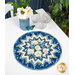 The completed Point of View Folded Star Table Topper colored in blue, green, and white fabrics from the Blue Harmony collection by Wilmington Prints. The topper is staged on a white table top with coordinating flowers, a blue butterfly, and three clear wine glasses.