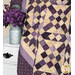 A closer look at the draped quilt, demonstrating fabric color and patchwork details; coordinating purple flowers accompany the quilt.