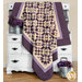 The completed Hummingbird Hill quilt, colored in rich cream and purple fabrics from the Plumberry III collection, artfully draped over a white armoire and staged with coordinating flowers.