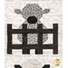A super close up on a patchwork lamb behind a fence, showing print and piecing details as well as top quilting details. 