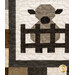 A super close up on a patchwork lamb behind a fence, showing print and piecing details as well as top quilting details. 