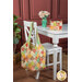 The completed Mondo Bag + Mini Charm Bag colored in vibrant, sunny colored fabrics from the Portofino collection by Moda, staged on a white chair and table in front of a maroon paneled wall.
