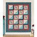 The completed Patchwork Porch quilt in ocean blue, brick red, and sandy cream fabrics from the Lighthouse collection by Andover Fabrics, staged on a cream wall with coordinating decor.
