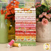 A stack of the fabrics included in the Peach Cobbler collection with vases and flowers and thread.
