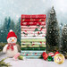 A stack of the fabrics included in The North Pole Flannel collection, with trees and snow and ornaments and a snowman plush and thread.
