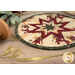 A shot of the round hot pad staged with a spool of sparkly gold ribbon and a sprig of mistletoe.