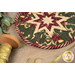 A shot of the round hot pad staged with a spool of sparkly gold ribbon and a sprig of mistletoe.