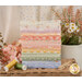 A stack of the fabrics included in the Pastel Prairie set, with a vase of flowers and clothes pins and thread.