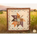 The Pressed Leaves quilt held up by someone standing behind it in a field at sunset.