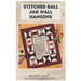 The front cover showing an showing the completed wall hanging pattern of a ball jar filled with sewing tools with a border of thread spools.