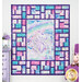 The completed Stained Glass Panel Quilt, colored in blue, pink, and white fabrics from the Sparkle Magic collection by Northcott Fabrics, hung on a lilac paneled wall and staged with coordinating unicorn decor.