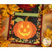 A close up on a jack-o-lantern block, framed by decorative fall leaves on a wooden tabletop.