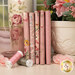 A stack of the fabrics in the Ruru Bouquet - Pink collection with a pot and a bottle and a cup and flowers and thread.