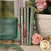 A stack of the fabrics included in the Ruru Bouquet - Green collection, with a pot and flowers and a cup.