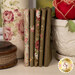 A stack of the fabrics included in the Ruru Bouquet - Brown collection, with a pot and flowers and a bottle and twine.