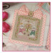 A image of the completed Spring Greetings cross stitch pattern staged with pink roses and finished with ribbon.