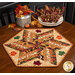 The completed 60 Degree Diamond Table Topper colored in warm fall fabrics from the Autumn Fields collection by Studio E Fabrics, staged on a wooden table with the cloth napkins in the same collection and coordinating decor.