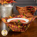 The completed bowl cozy colored in warm autumn themed fabrics from the Autumn Fields collection by Studio E Fabrics, staged on a wooden table, holding a white owl with tomato soup inside. The other bowl cozies and coordinating decor can be seen in the background.