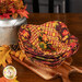 Three nested bowl cozies in warm autumn themed fabrics, staged on a wooden cutting board on a mahogany table with coordinating decor..