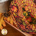 Three nested bowl cozies in warm autumn themed fabrics, staged on a wooden cutting board on a mahogany table.