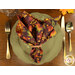 A top down shot of a table setting with a green plate, gold tableware, and the napkin with the dark purple fabric with an autumn leaf print facing outward.