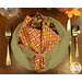 A top down shot of a table setting with a green plate, gold tableware, and the napkin with a fancy golden yellow and rustic red plaid design print facing outward.