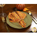 An angled shot of a table setting with a green plate, gold tableware, and the napkin with a fancy golden yellow and rustic red plaid design print facing outward.