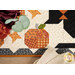A stylized top down close up on the runner, showing fabric details on a patchwork pumpkin as coordinating flowers peek into frame from the upper left corner.