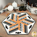 The completed 60 Degree Diamond Table Topper, colored in gray, orange, and white fabrics from the Agatha Road collection from Moda Fabrics, staged on a wooden table with coordinating Halloween decor.